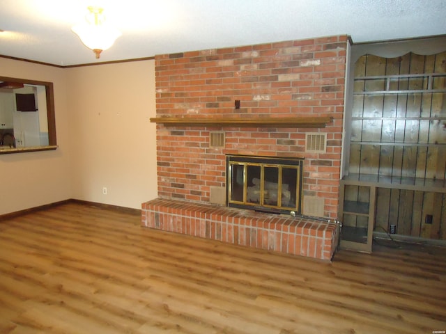 unfurnished living room with a fireplace, wood finished floors, visible vents, baseboards, and crown molding