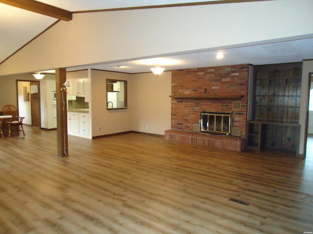 unfurnished living room with a fireplace, visible vents, lofted ceiling with beams, wood finished floors, and baseboards