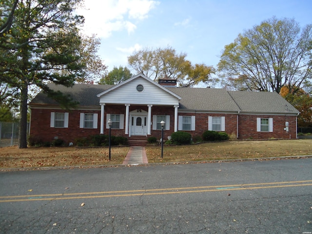 greek revival house featuring a porch, a front yard, brick siding, and roof with shingles