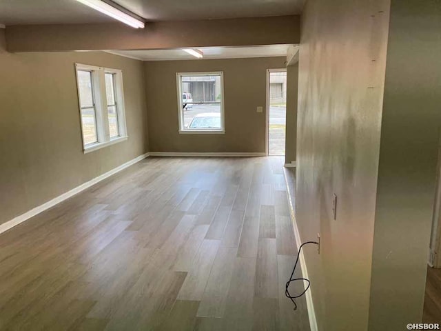 spare room featuring light wood-style flooring, baseboards, and beamed ceiling