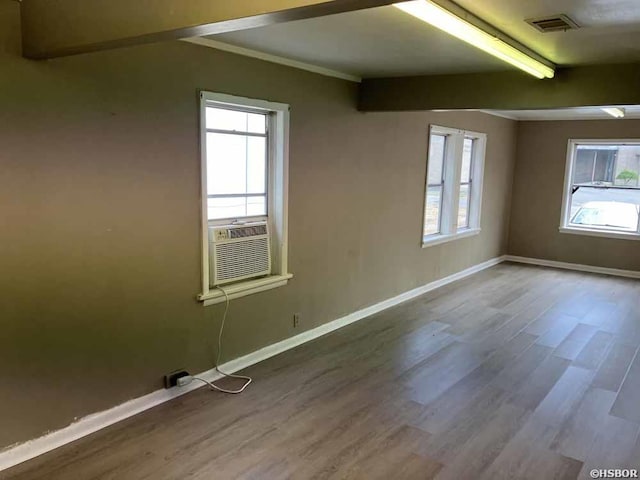 unfurnished room featuring cooling unit, wood finished floors, visible vents, baseboards, and beam ceiling