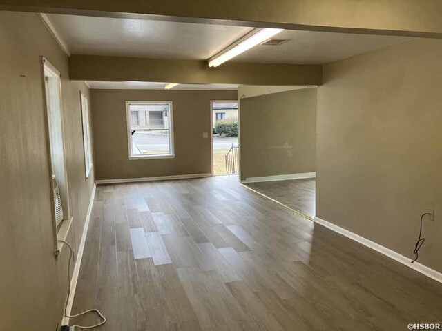 spare room with visible vents, wood finished floors, beam ceiling, and baseboards