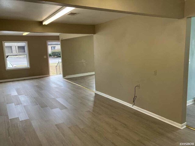 spare room featuring beam ceiling, wood finished floors, visible vents, and baseboards