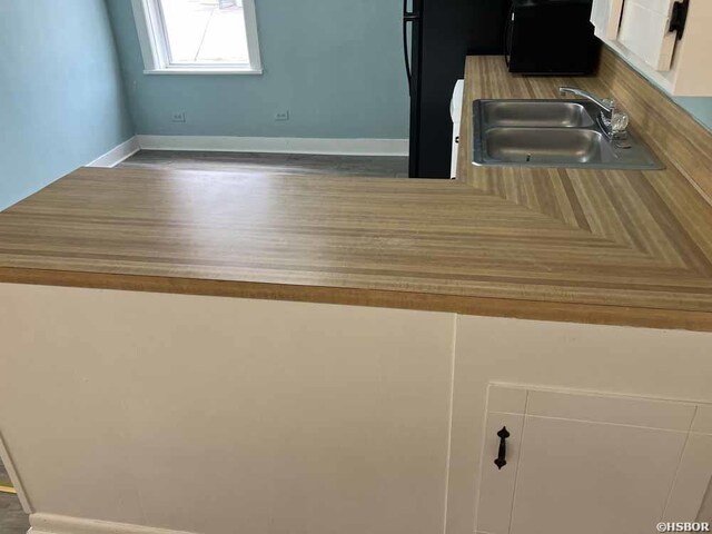 kitchen with light countertops, a sink, white cabinetry, and baseboards