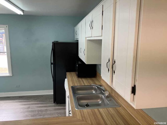 kitchen with light wood finished floors, baseboards, light countertops, white cabinetry, and a sink