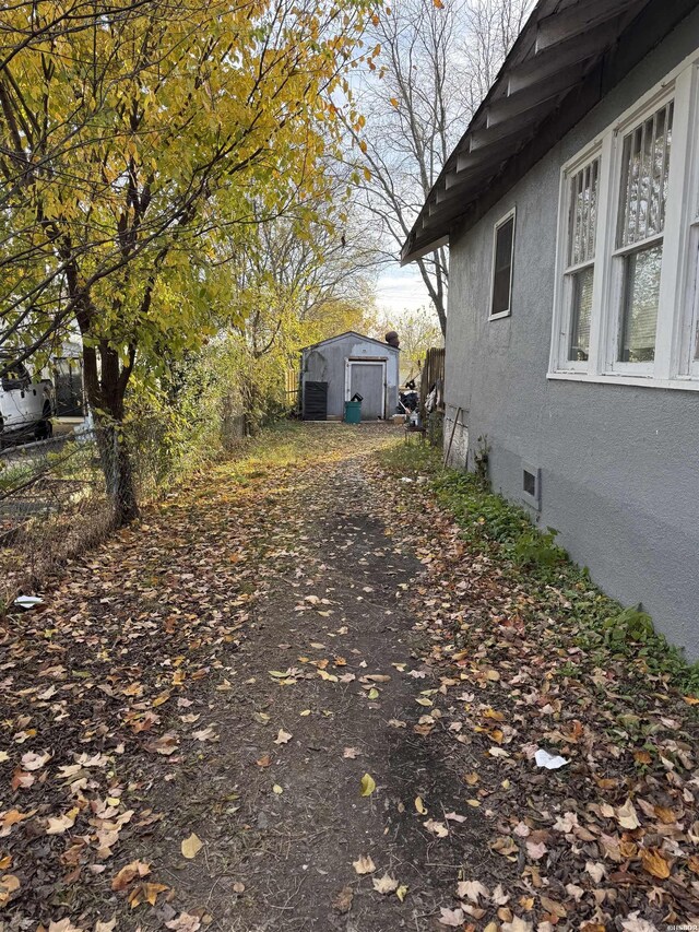 view of property exterior featuring a storage shed, fence, an outbuilding, and stucco siding