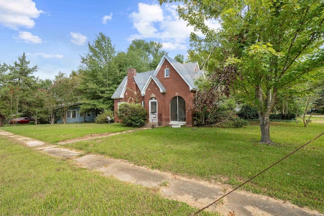 view of front of house featuring brick siding, a chimney, and a front lawn