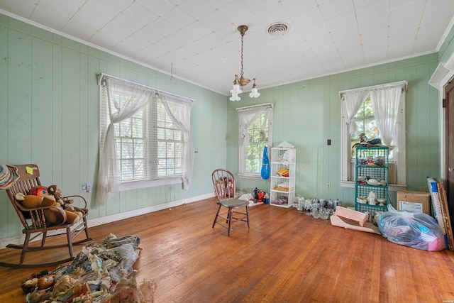 living area featuring visible vents, baseboards, wood finished floors, crown molding, and a notable chandelier