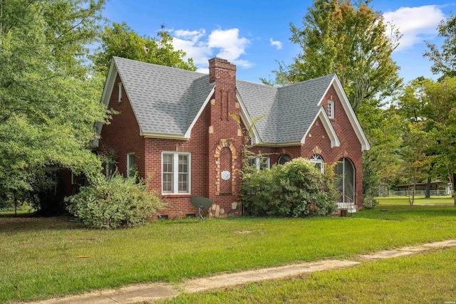 tudor house with brick siding, a chimney, a shingled roof, and a front lawn