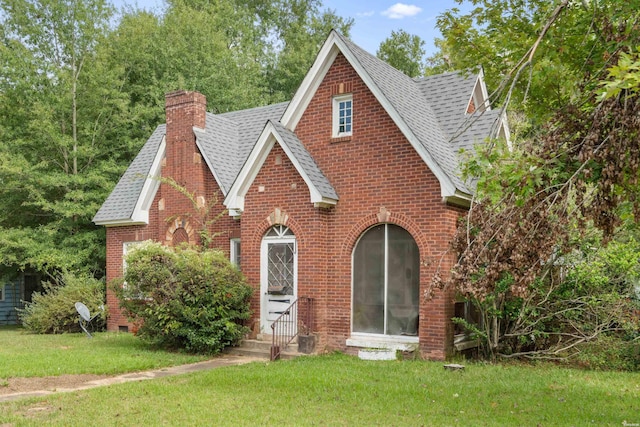 tudor-style house featuring entry steps, a shingled roof, a chimney, and brick siding