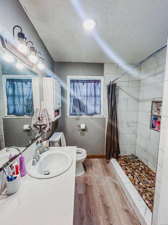 bathroom featuring a textured ceiling, toilet, wood finished floors, baseboards, and a shower stall