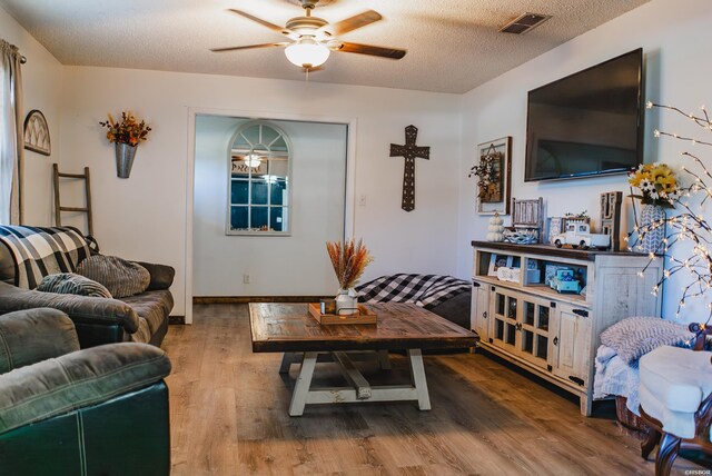 living area with a textured ceiling, visible vents, wood finished floors, and a ceiling fan