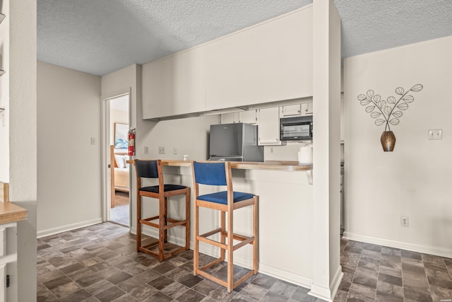 5371 Central Ave Unit 5H, Hot Springs, AR 71913 - kitchen with freestanding refrigerator, black microwave, a textured ceiling, a kitchen breakfast bar, and stone finish floors