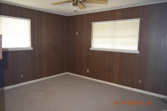 empty room with ceiling fan, ornamental molding, wood walls, and baseboards