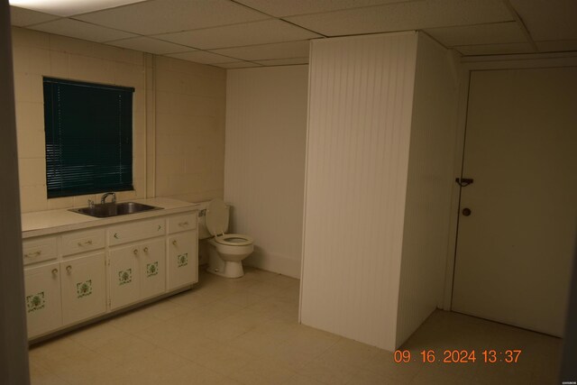 bathroom with toilet, a drop ceiling, concrete block wall, and tile patterned floors