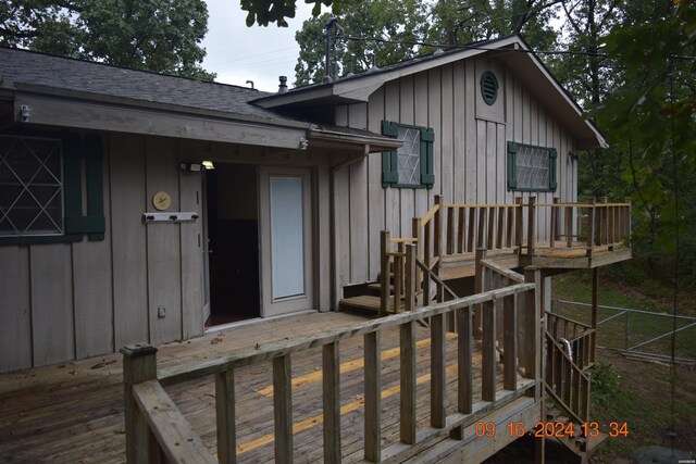 exterior space with a deck, a shingled roof, board and batten siding, and fence