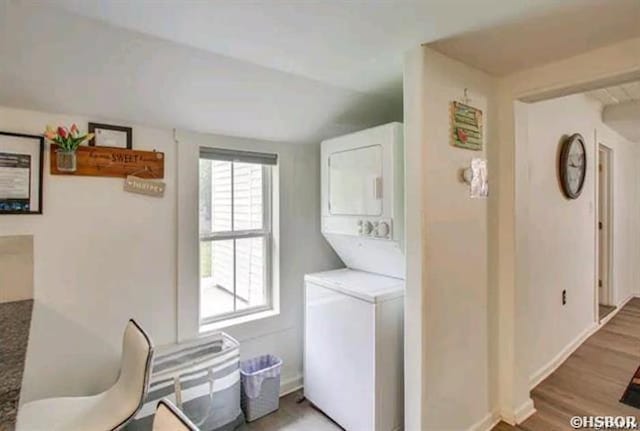 washroom featuring stacked washer and dryer, laundry area, baseboards, and light wood finished floors