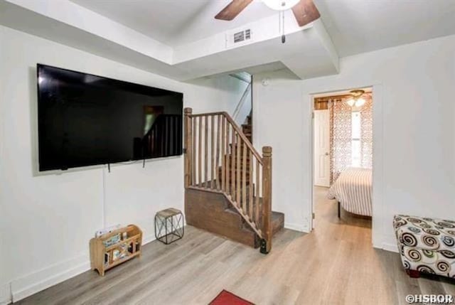 living area featuring a ceiling fan, visible vents, stairway, and wood finished floors