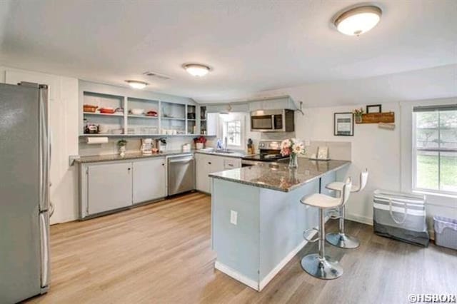 kitchen with a peninsula, light wood-style floors, appliances with stainless steel finishes, and open shelves