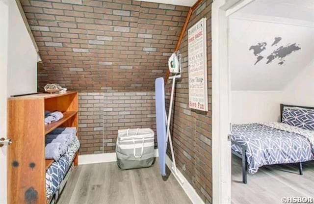 bedroom with baseboards, brick wall, and wood finished floors