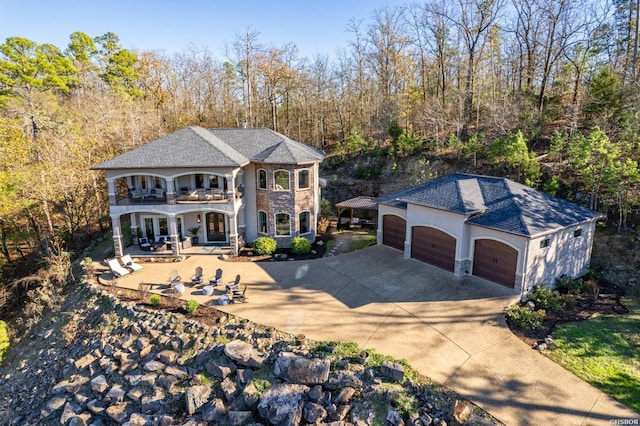 view of front of home featuring a garage, concrete driveway, a patio, stone siding, and stucco siding