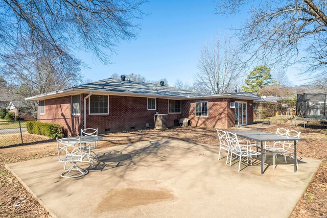 rear view of house with a trampoline, crawl space, brick siding, and a patio