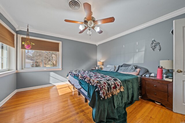 bedroom with light wood-style flooring, visible vents, a ceiling fan, baseboards, and crown molding