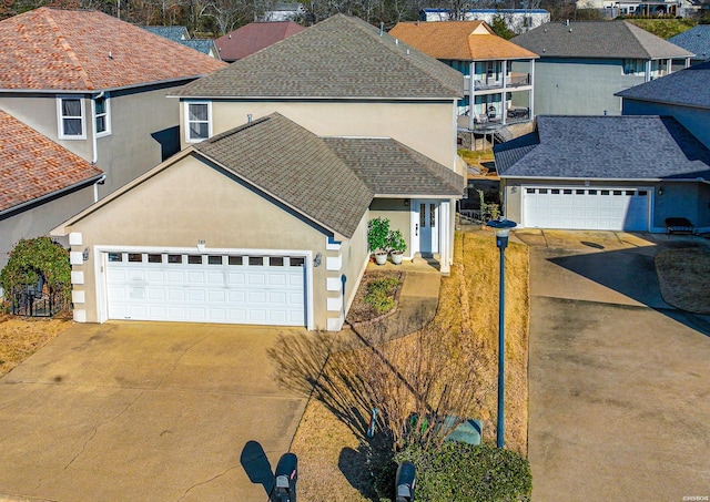 traditional-style house with a shingled roof, concrete driveway, a residential view, an attached garage, and stucco siding