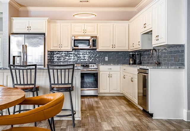 kitchen featuring crown molding, appliances with stainless steel finishes, light wood-style floors, white cabinets, and light stone countertops