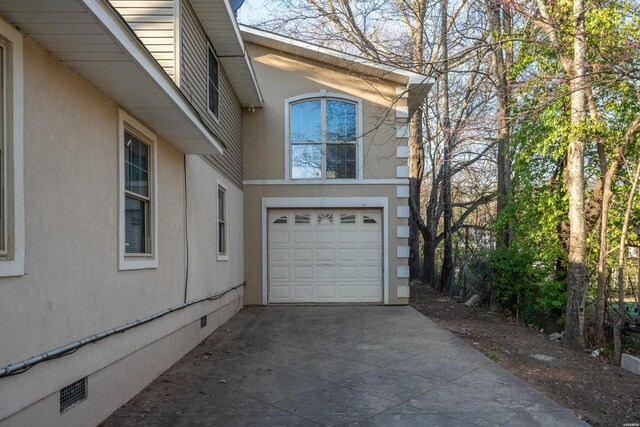 view of side of home featuring crawl space, an attached garage, driveway, and stucco siding