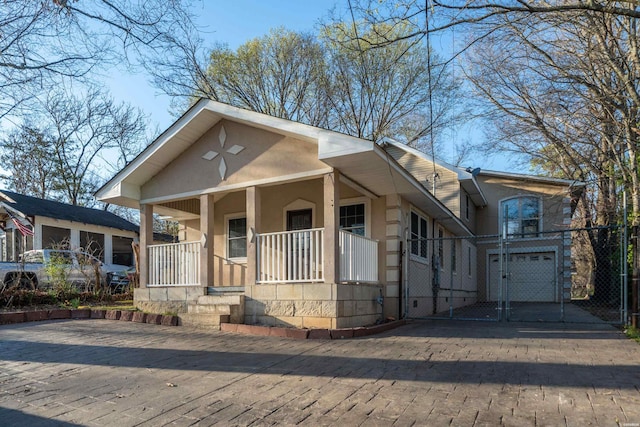 bungalow-style house with a garage, covered porch, driveway, and stucco siding