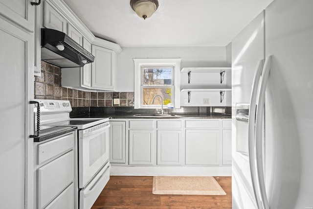 kitchen featuring under cabinet range hood, a sink, dark countertops, dark wood-style floors, and white appliances