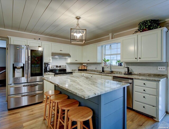 kitchen with pendant lighting, stainless steel appliances, white cabinets, a kitchen island, and under cabinet range hood