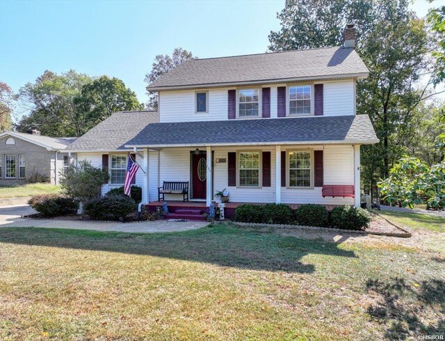 traditional-style home with covered porch, a shingled roof, a chimney, and a front yard