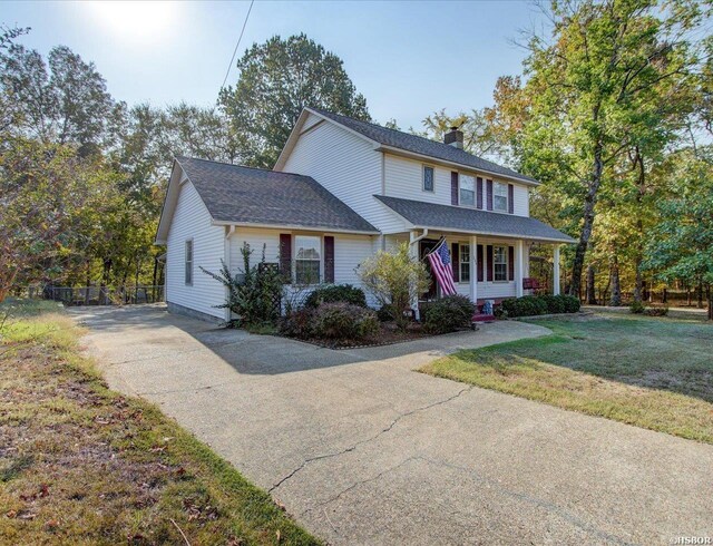 view of front of house with driveway, a chimney, covered porch, fence, and a front yard