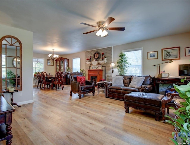 living area featuring plenty of natural light, ceiling fan with notable chandelier, a brick fireplace, and light wood-style floors