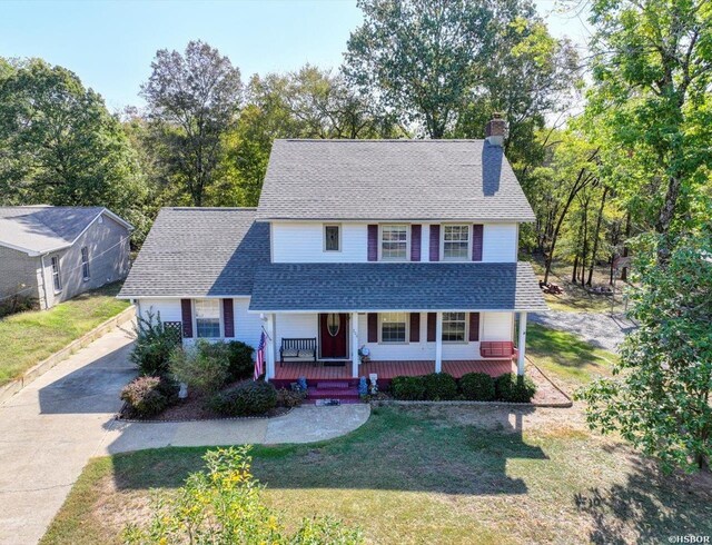 view of front of house with a chimney, a front lawn, roof with shingles, and a porch