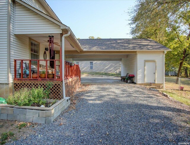 exterior space featuring a shingled roof, a ceiling fan, gravel driveway, a porch, and a carport