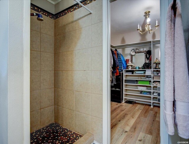 bathroom featuring a spacious closet, wood finished floors, a shower stall, and an inviting chandelier