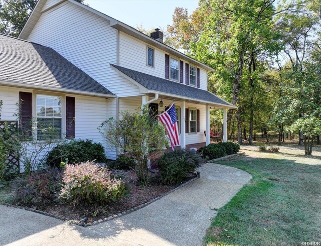 view of front of home with covered porch, a shingled roof, a chimney, and a front yard