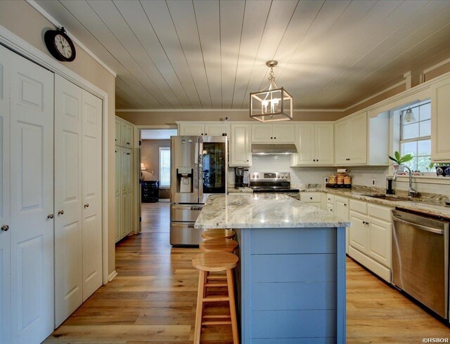 kitchen featuring hanging light fixtures, appliances with stainless steel finishes, a sink, a kitchen island, and under cabinet range hood