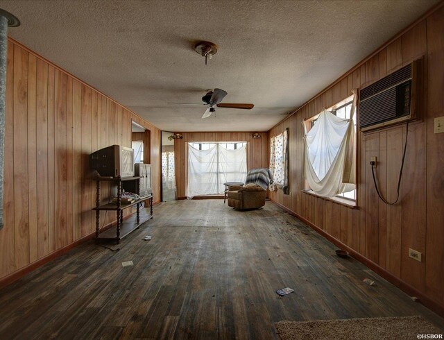 unfurnished living room featuring a textured ceiling, a ceiling fan, dark wood-style flooring, and a wall mounted air conditioner