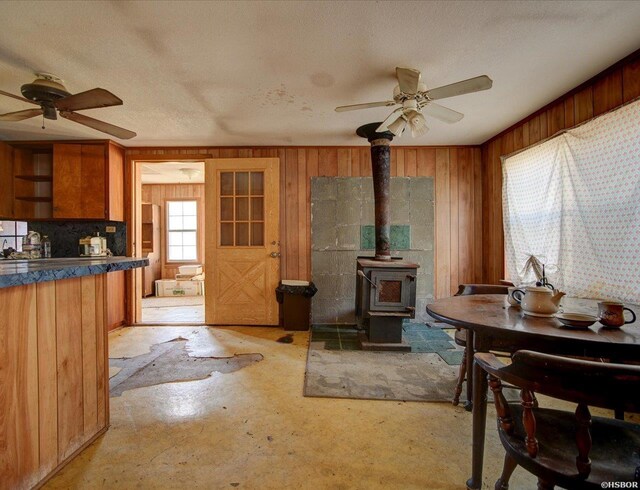 kitchen with a wood stove, ceiling fan, wooden walls, and a textured ceiling