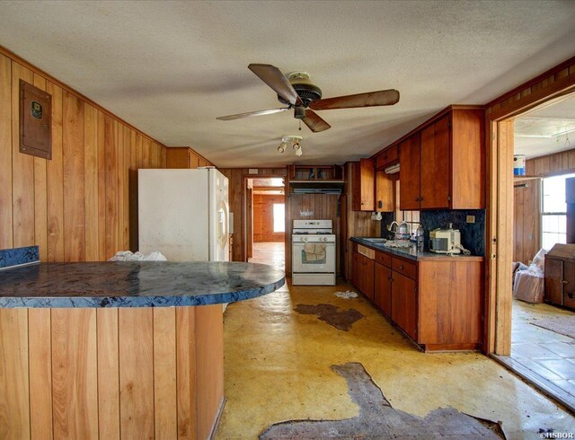 kitchen with dark countertops, wooden walls, white appliances, a peninsula, and under cabinet range hood