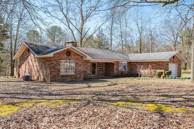 ranch-style home featuring brick siding, a chimney, and central AC