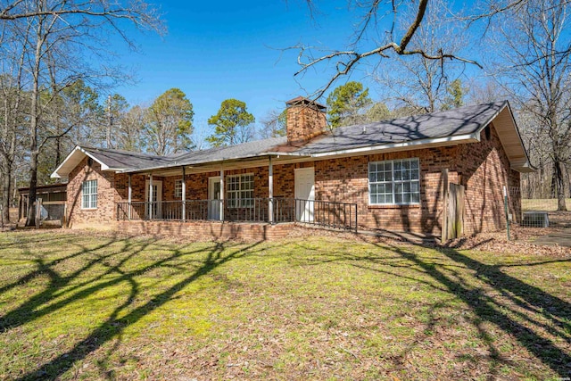 back of property with brick siding, covered porch, a chimney, and a yard