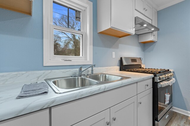 kitchen featuring gas stove, white cabinetry, a sink, and wall chimney exhaust hood