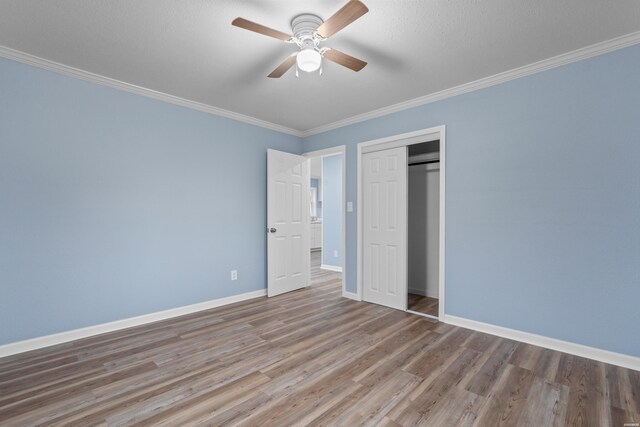 unfurnished bedroom featuring crown molding, a closet, ceiling fan, wood finished floors, and baseboards