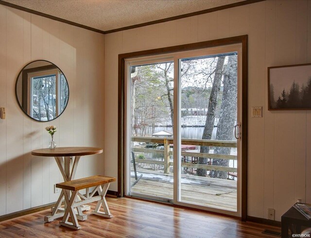 doorway with baseboards, visible vents, wood finished floors, crown molding, and a textured ceiling