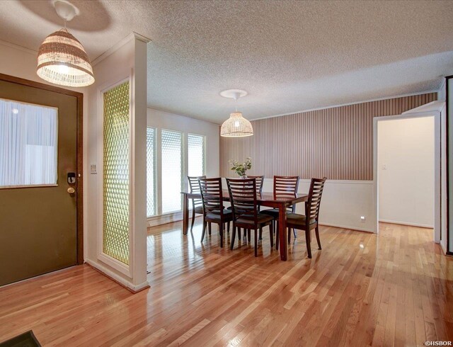 dining room featuring light wood-type flooring, crown molding, and a textured ceiling